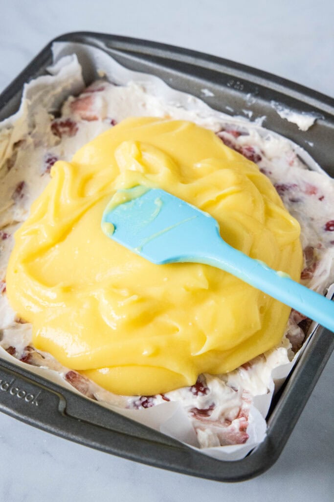 spreading pudding over cream cheese and strawberry layer in a baking dish