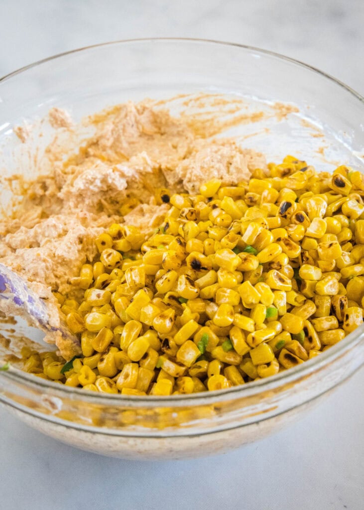 Corn kernels added to dip ingredients in a glass bowl.