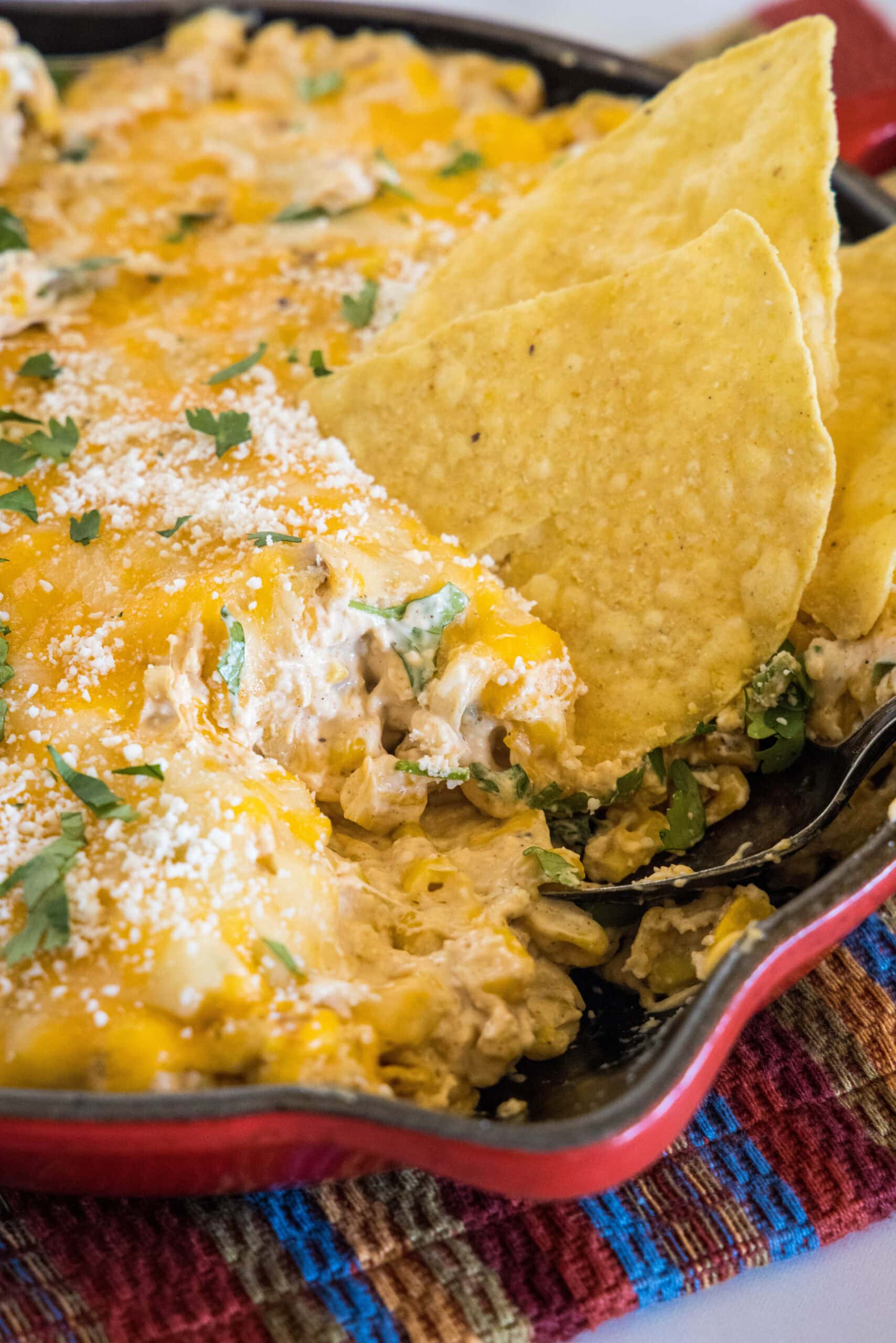 A tortilla chip dipped into a skillet of cheesy street corn dip.
