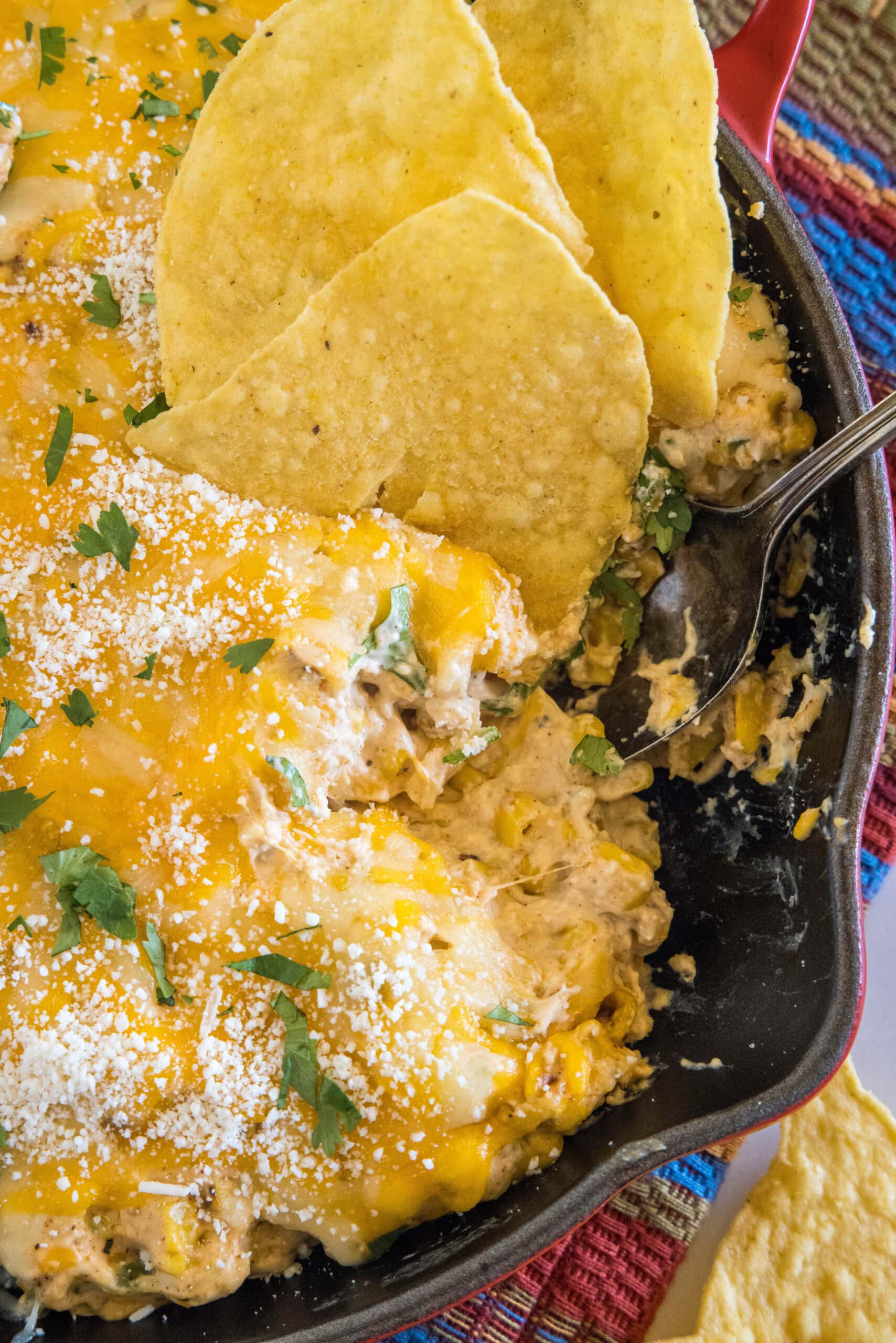 A tortilla chip dipped into a skillet of cheesy street corn dip.