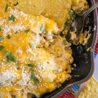 Close up of a tortilla chip dipped into a skillet of cheesy street corn dip.