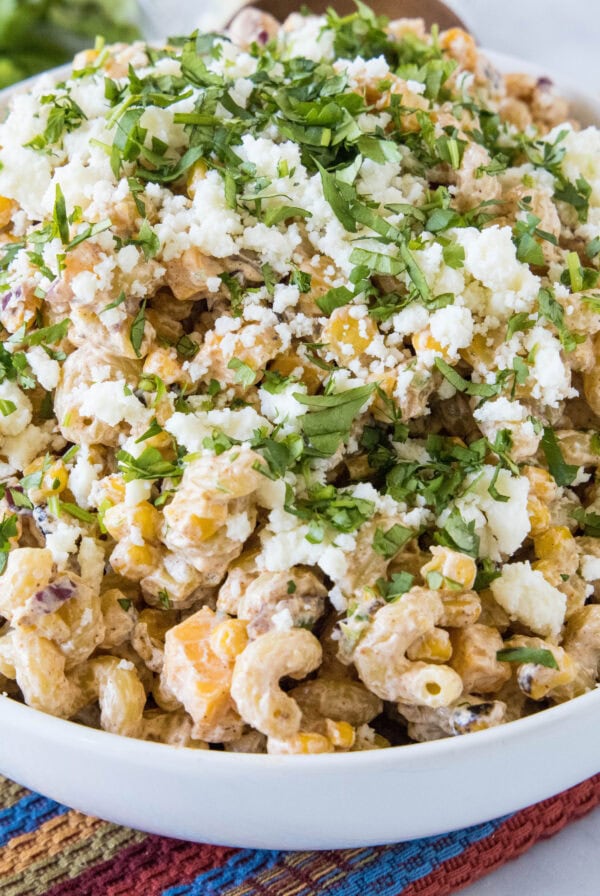 A bowl of Mexican street corn pasta salad garnished with Cotija cheese and cilantro.