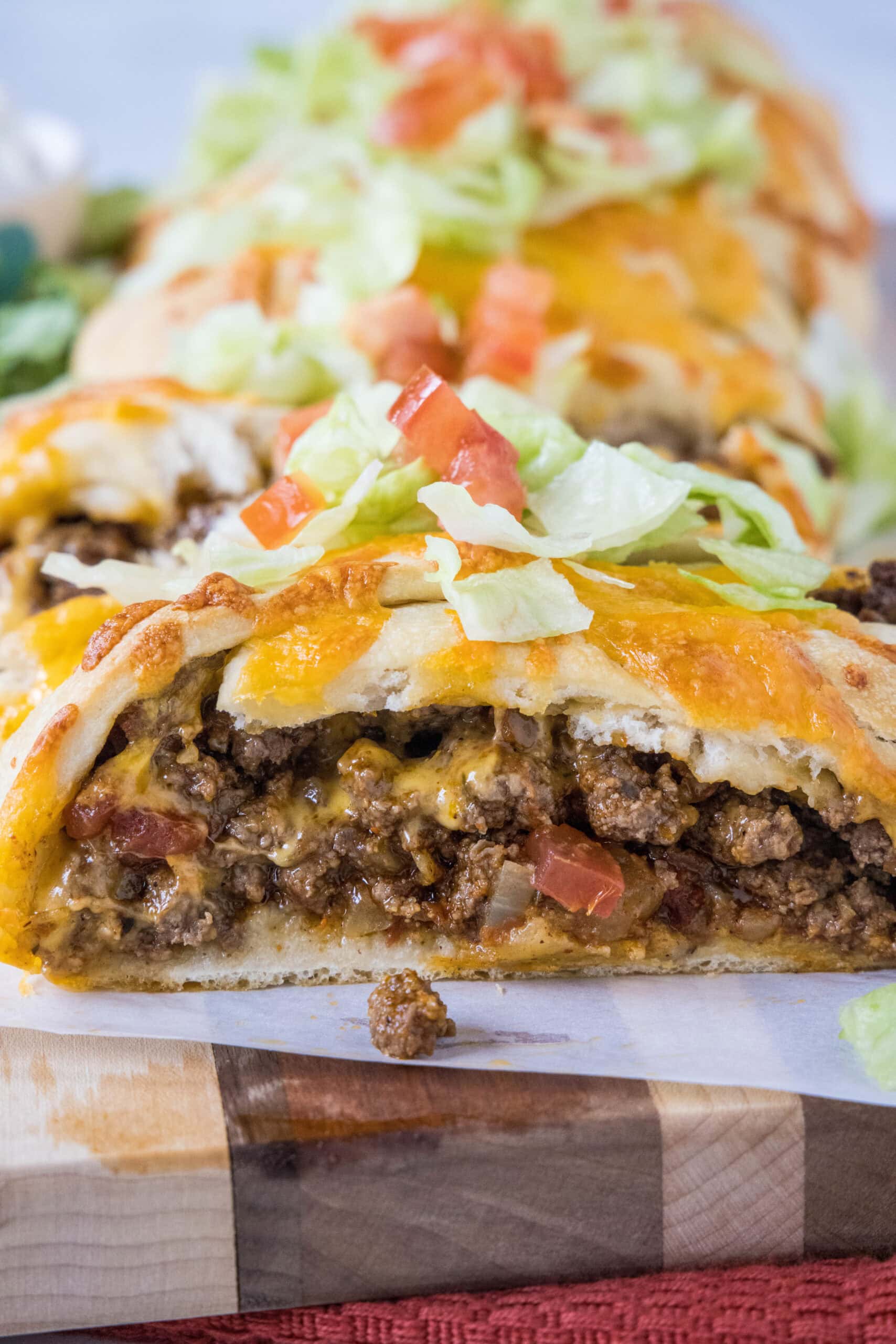 Close up of a taco braid filled with ground beef and topped with melted cheese, shredded lettuce, and diced tomatoes.