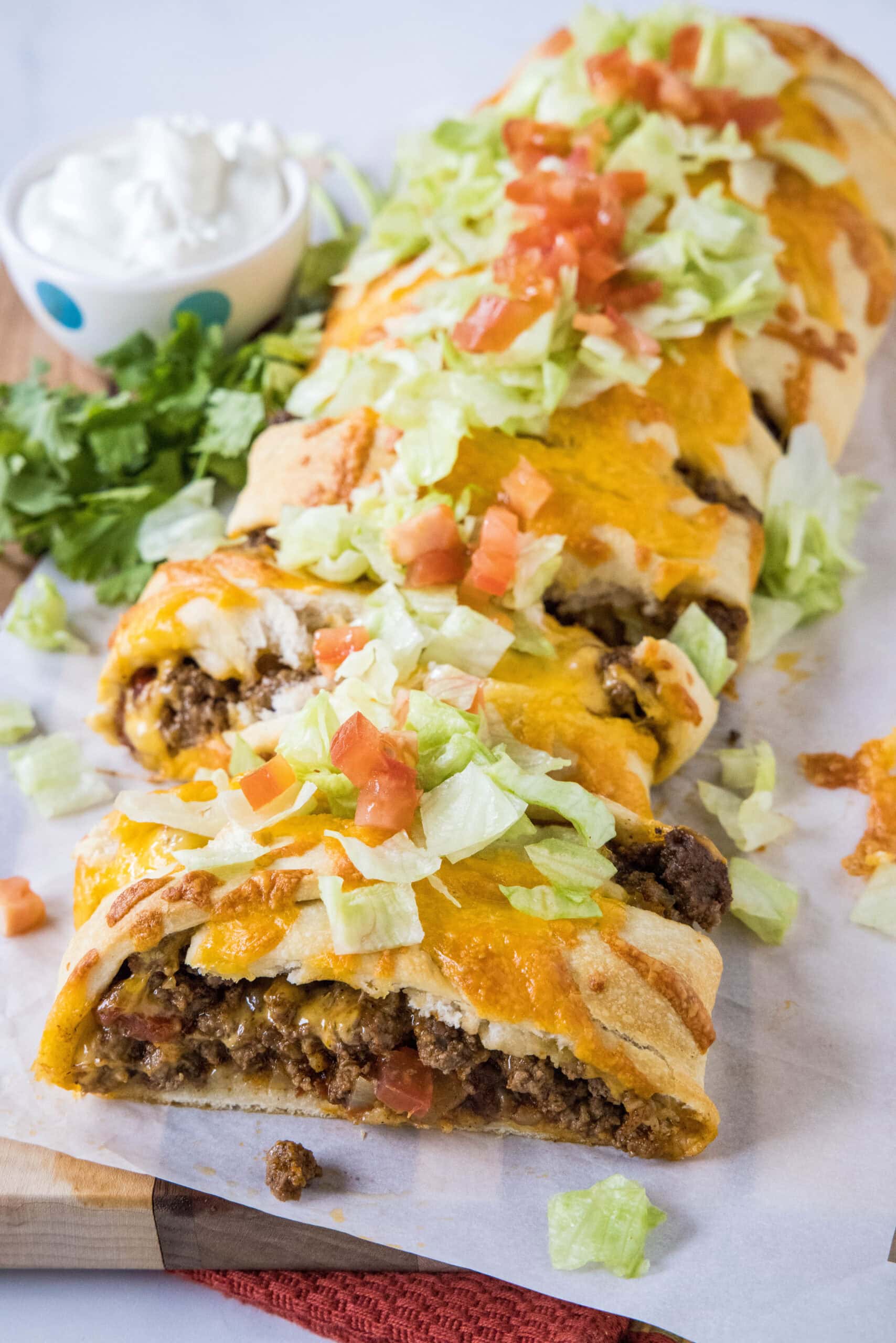Overhead view of a taco braid cut into slices, filled with ground beef and topped with melted cheese, shredded lettuce, and diced tomatoes.