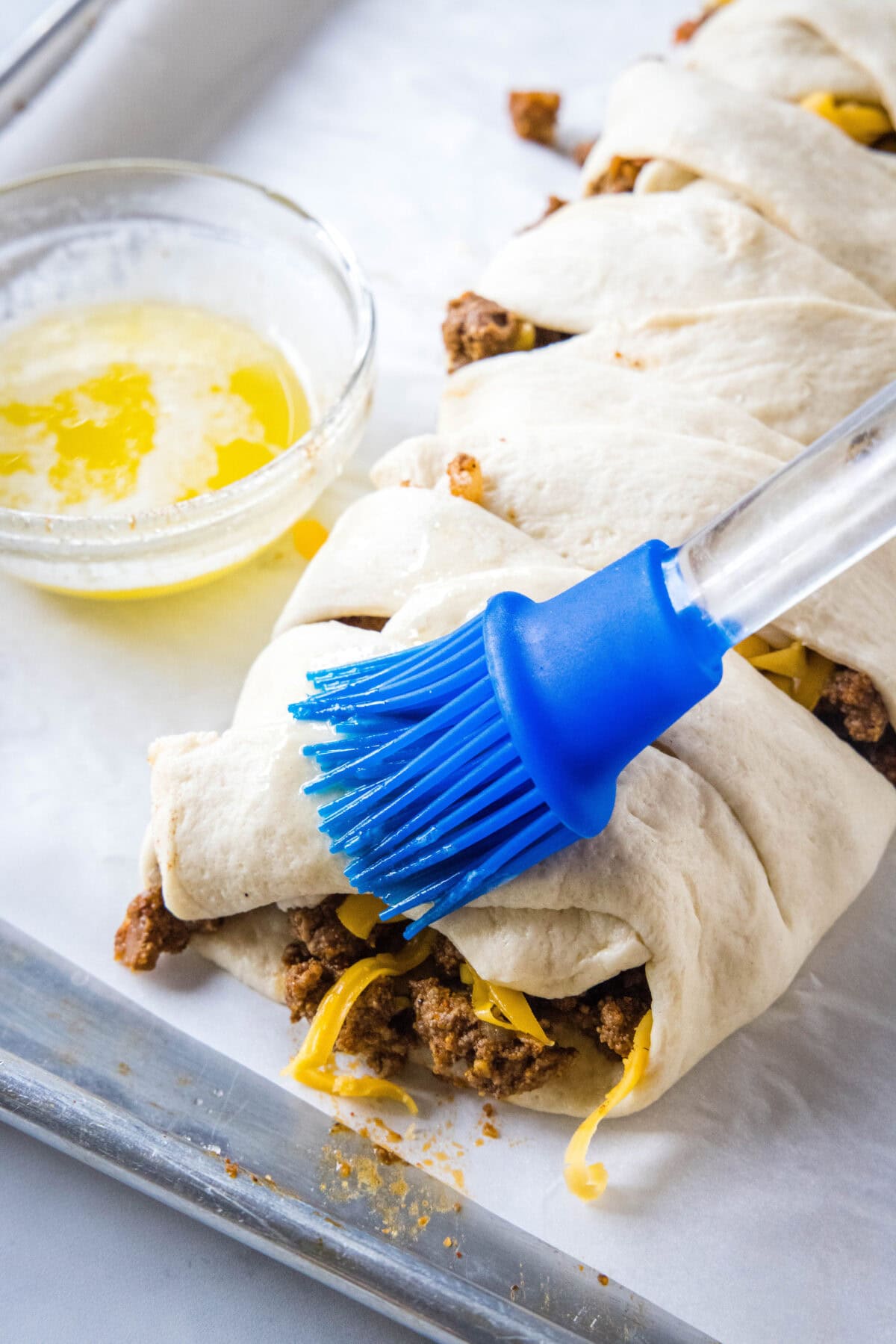 A rubber brush is used to brush the top of the taco braid with melted butter.