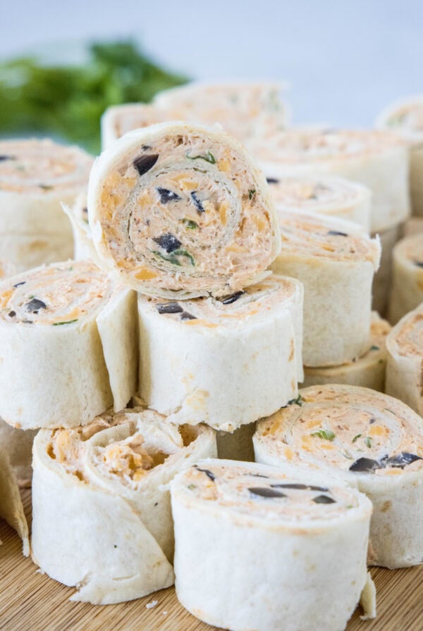 Taco pinwheels stacked in a pile on a wooden cutting board.