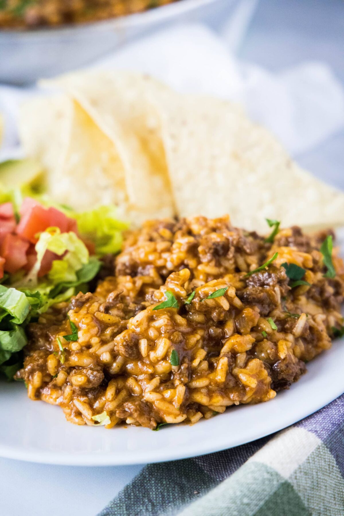 A plate with taco rice, topped with lettuce and cilantro, with tortilla chips on the side