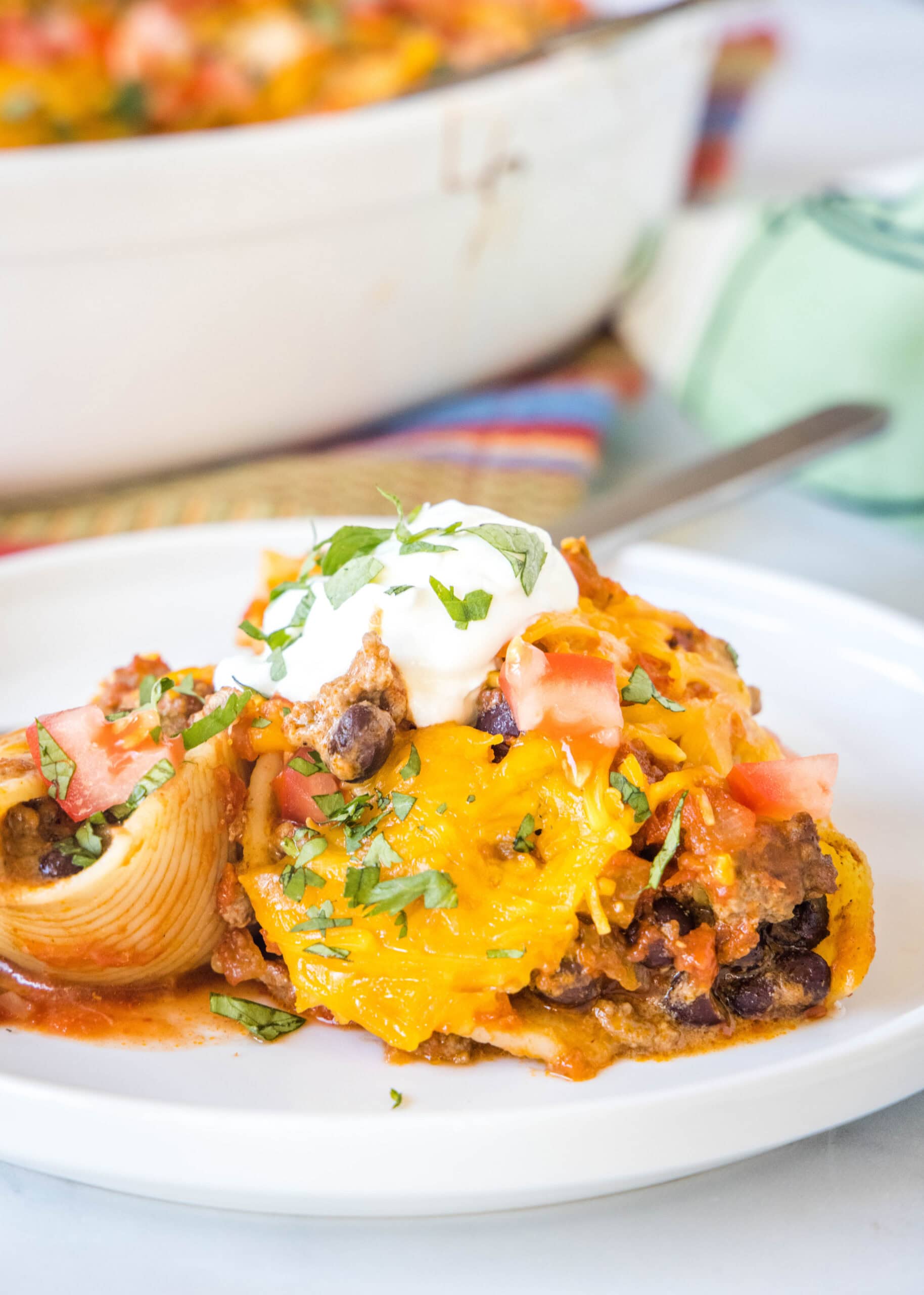 A serving of taco stuffed shells on a white plate next to a fork.