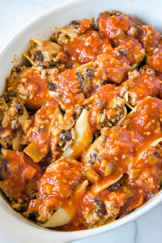 Assembled taco stuffed shells covered with salsa in a baking dish.