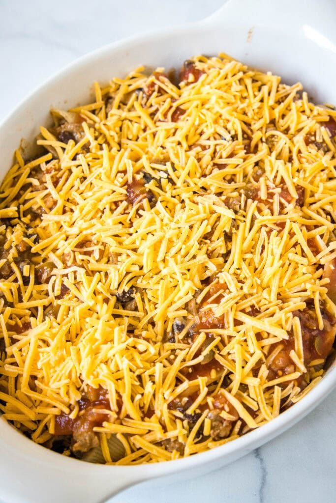 Assembled taco stuffed shells covered with salsa and shredded cheese in a baking dish.