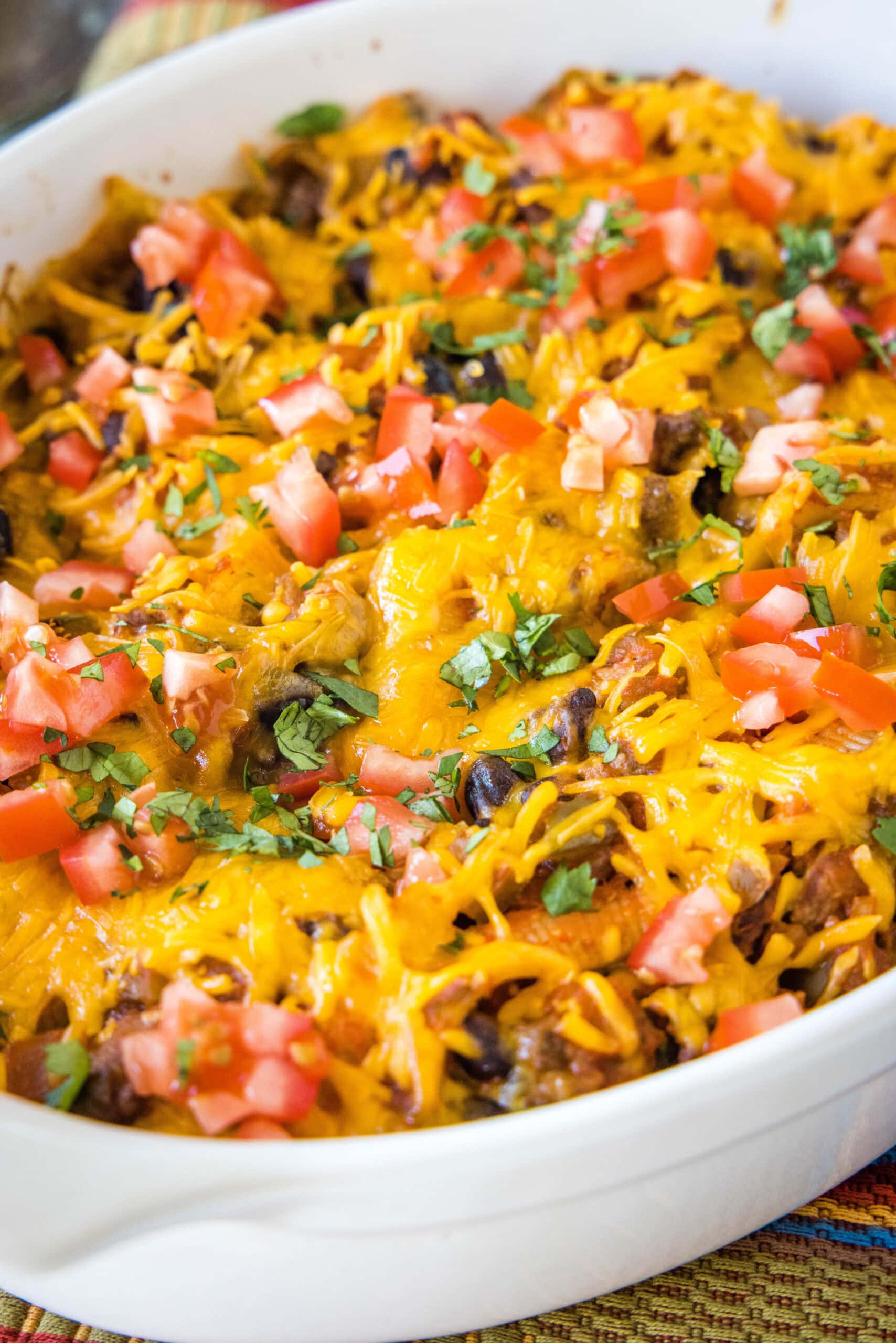 Baked taco stuffed shells in a baking dish garnished with diced tomatoes and cilantro.