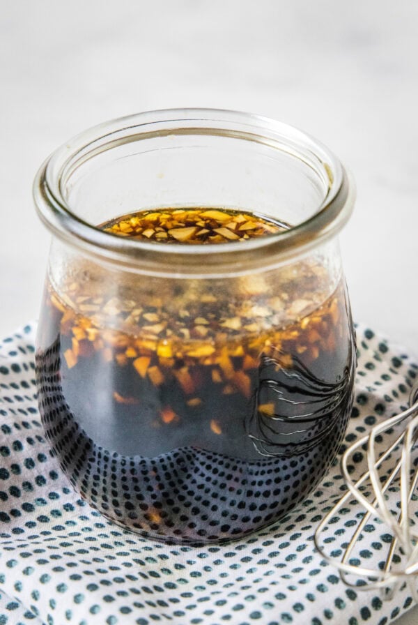 Homemade teriyaki sauce in a glass jar on a blue and white polka dot napkin, next to a whisk.