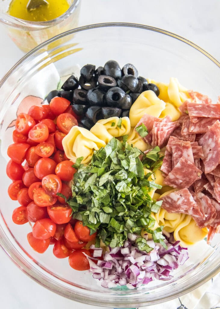 Tortellini salad ingredients combined in a glass bowl.
