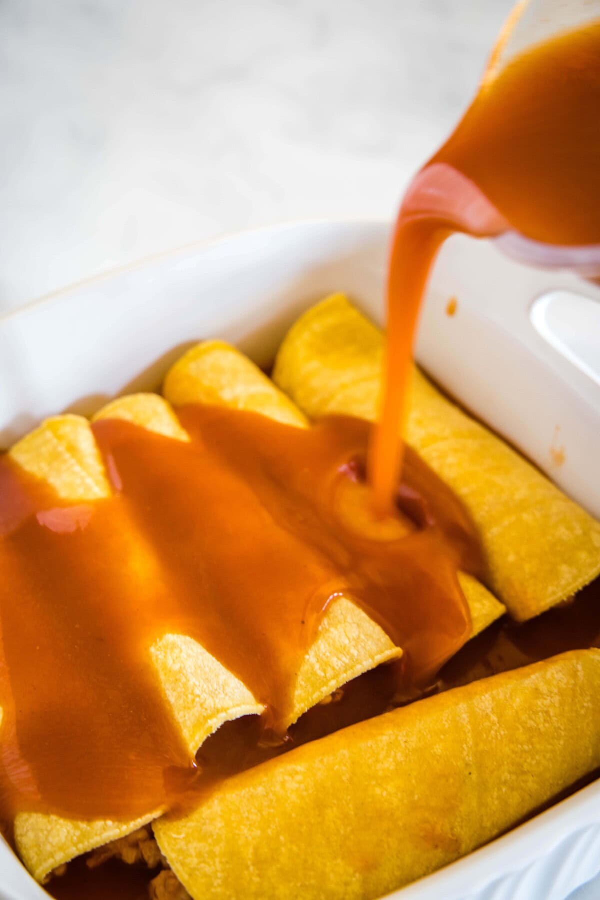 pouring enchilada sauce over rolled enchiladas
