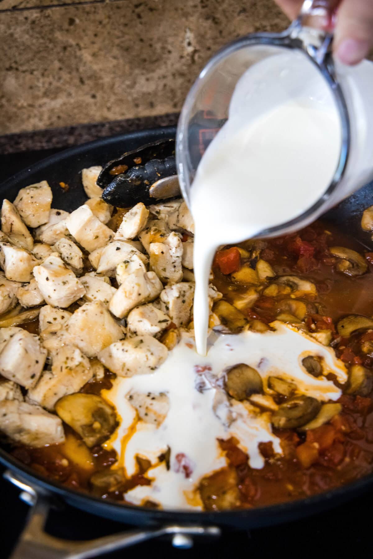 pouring cream into skillet with chicken and tomatoes