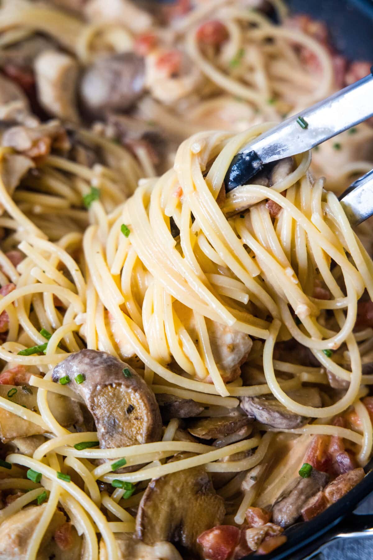 tongs scooping pasta out of a skillet