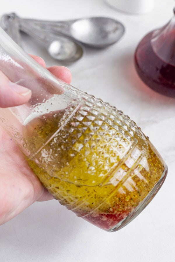 A hand holding up a carafe of red wine vinaigrette.